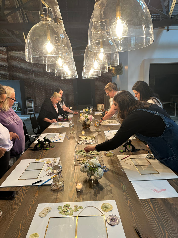 A workshop with people designing pressed floral frames on a long wooden table.