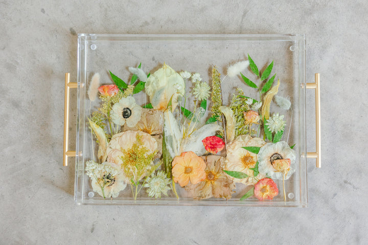 Pressed flowers designed into a functional resin serving tray against a cement backround. 