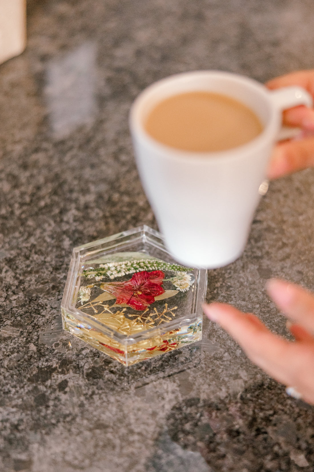 A cup of coffee is set on top of a pressed flower ring dish . 