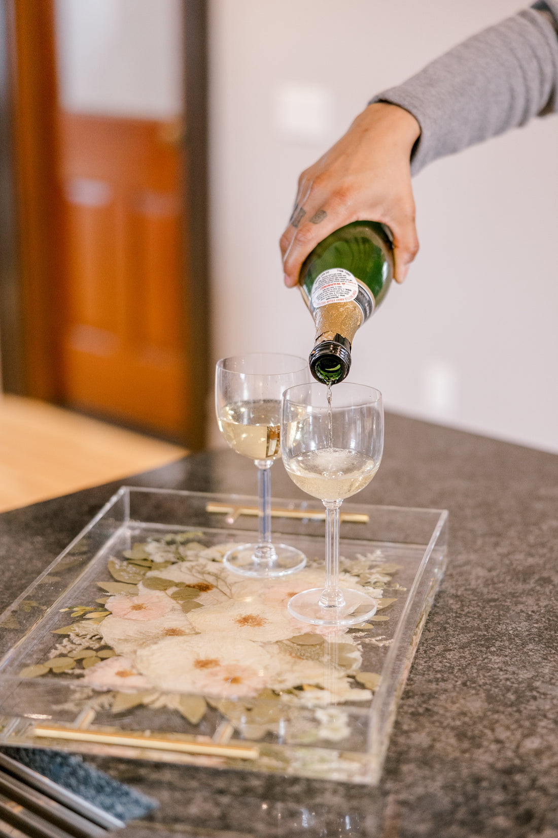 Pouring champagne into a custom pressed flower serving tray on a kitchen island. 