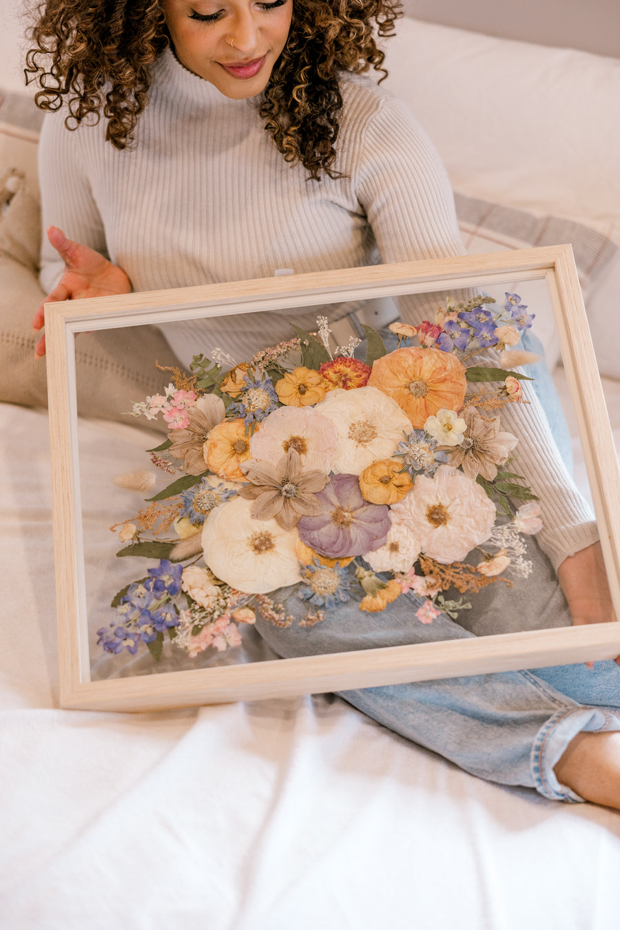 Beautiful pressed florals displayed in a floating glass frame held by a bride admiring her bouquet preservation.