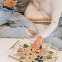 A couple happily uses their pressed floral serving tray while sitting on their bed.