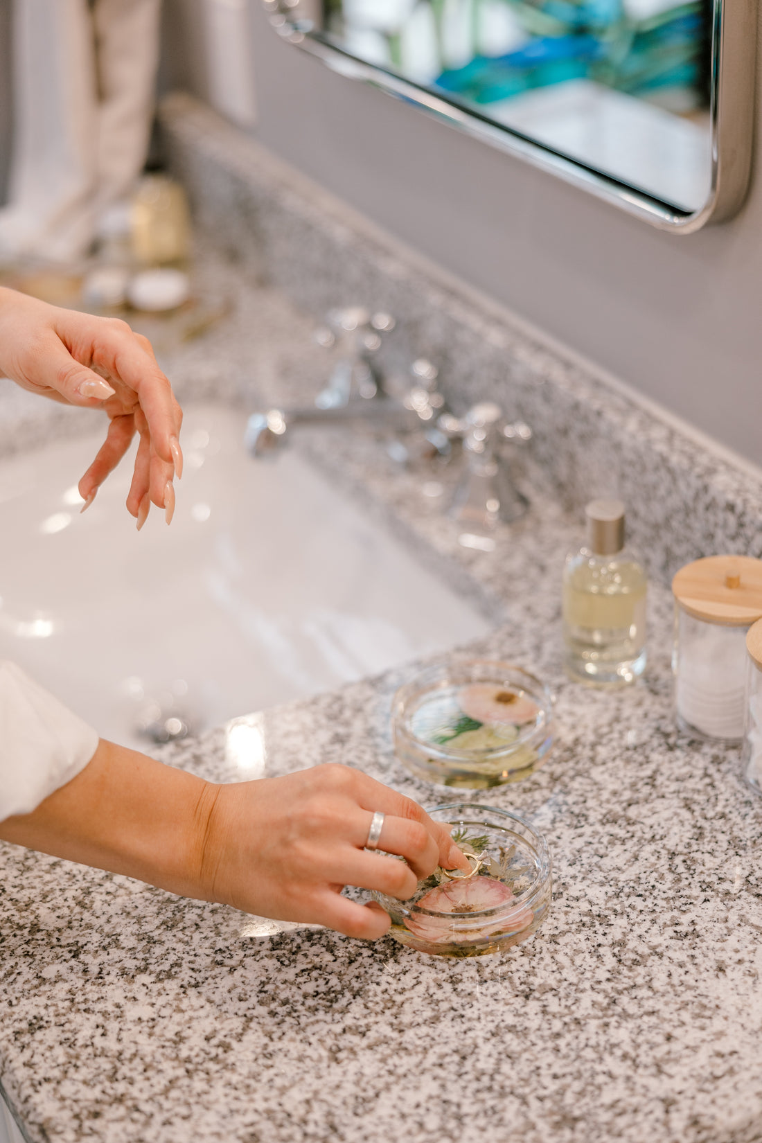 A woman removes her earrings and set them inside a circle ring dish on her bathroom vanity. 