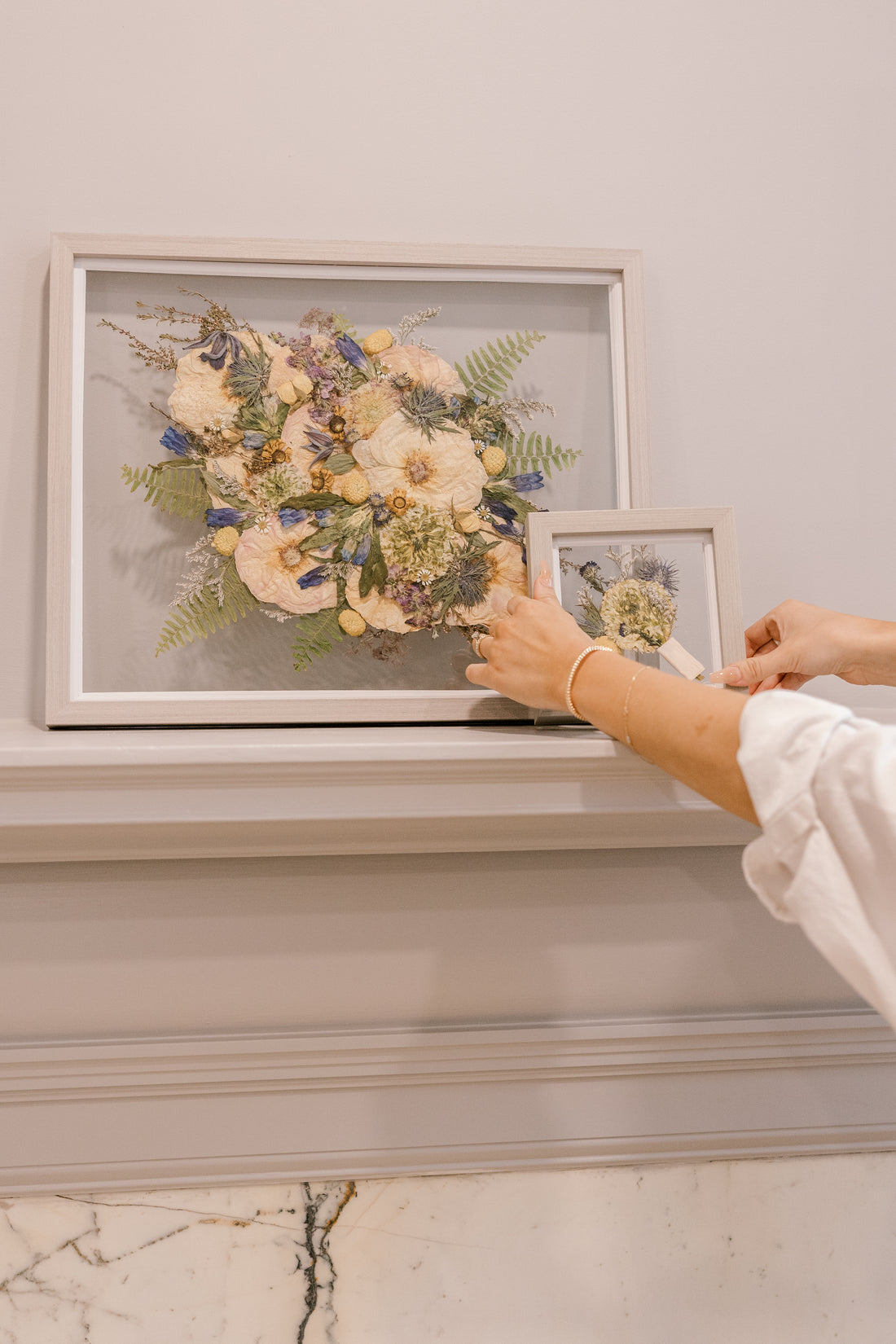 Two grey wood pressed floral frames are displayed on a mantle to be showcased in their home.
