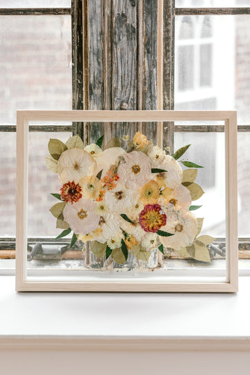 Pressed flowers and pressed florals in a natural wood float frame featuring pressed roses, pressed dahlias, pressed ranunculus, and pressed greenery. 