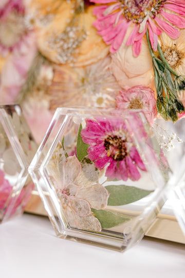 A hexagon shaped pressed floral ring dish sits aside a background of pressed and framed florals. 