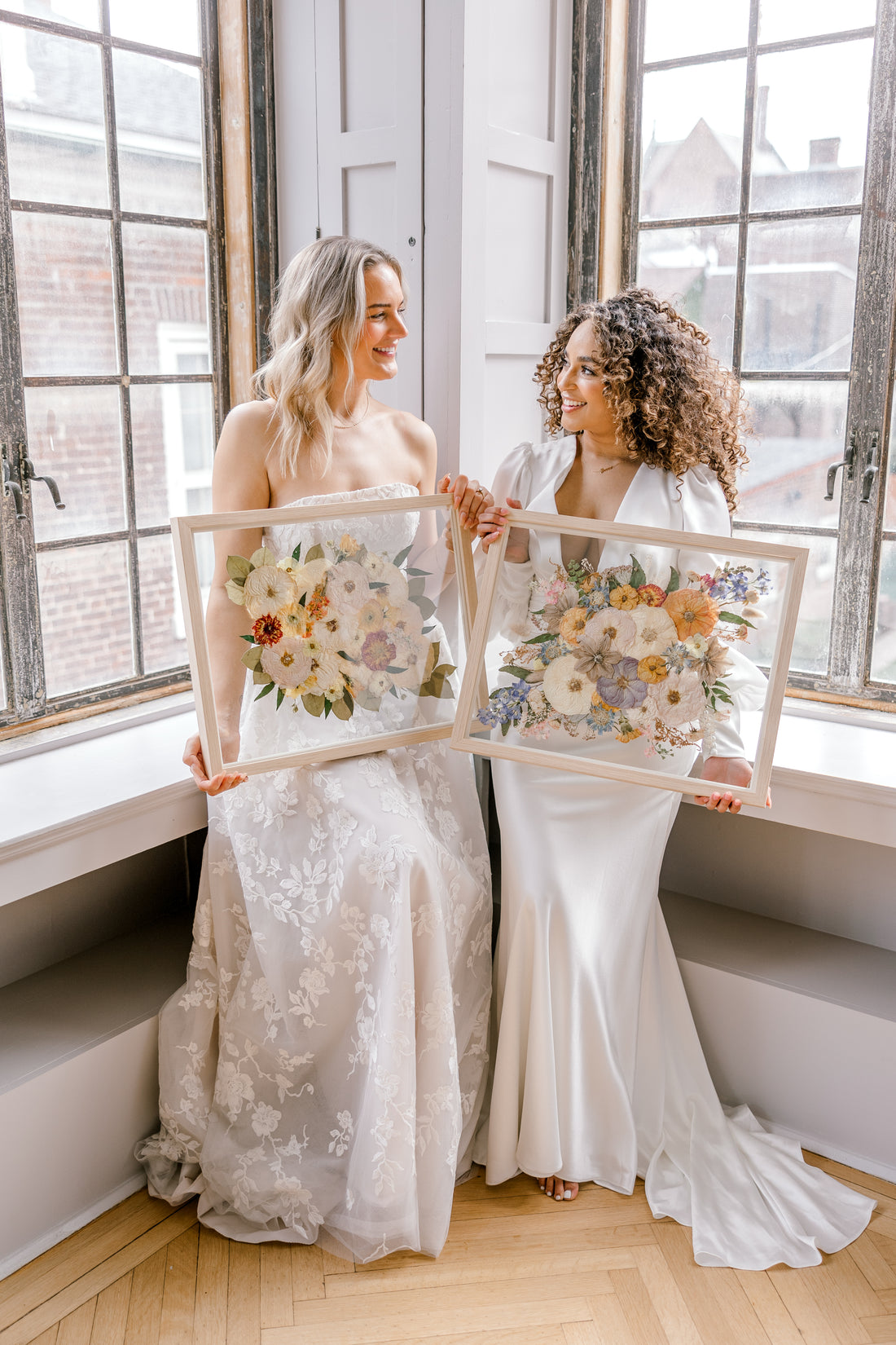 Two brides happily holding their pressed flower preservation pieces, smiling at each other and the lifetime of memories they will hold. 