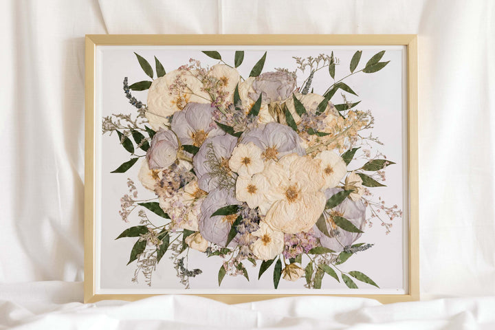 A pressed flower bouquet preserved in a glass frame with a gold wood surround, made by Element Preservation (Element Design Co.)