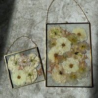 a small and big gold hanging frame encased with pressed flowers in a beautiful burst design against a white rug.