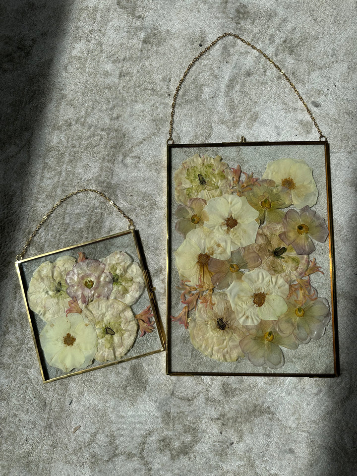 a small and big gold hanging frame encased with pressed flowers in a beautiful burst design against a white rug.