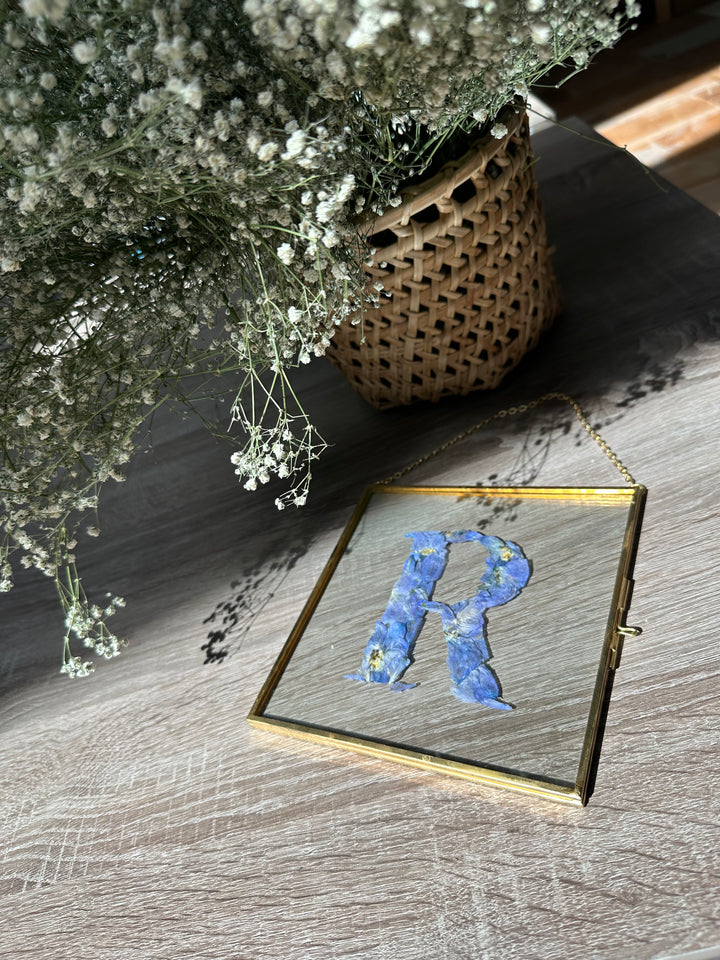 square gold hanging frame with blue pressed flowers. 