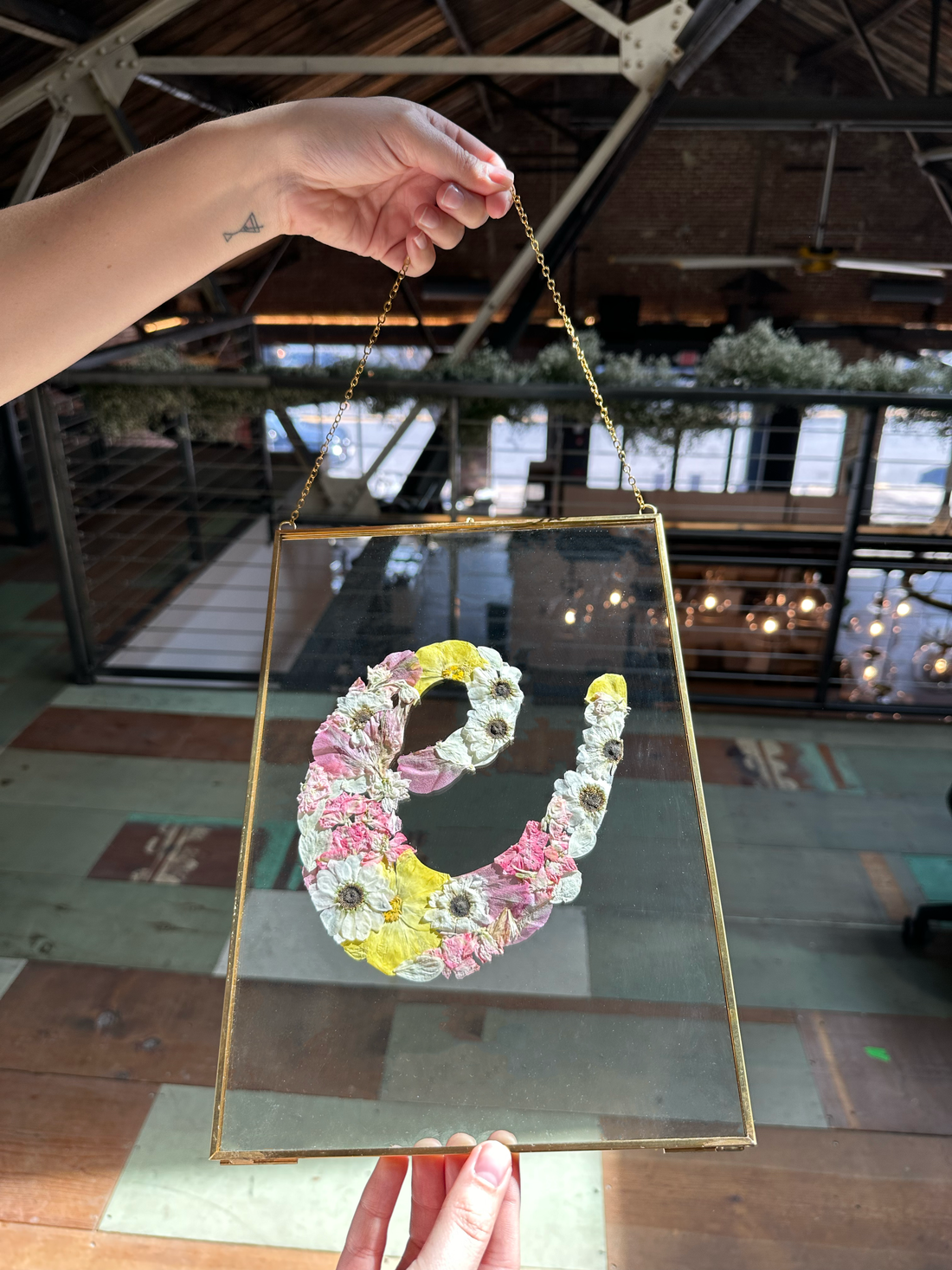 a big gold ganging frame designed with springy blooms in the shape of the letter e being held by someone.
