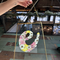 a big gold ganging frame designed with springy blooms in the shape of the letter e being held by someone.