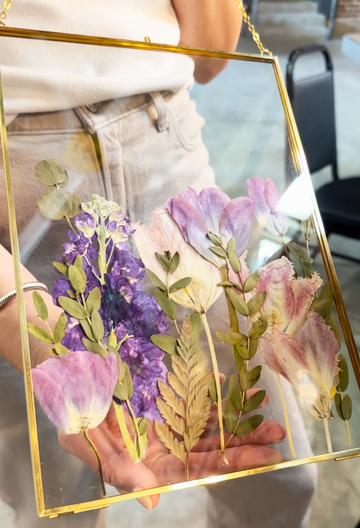gold hanging frame with purple pressed florals being held by a person that designed it at a workshop.