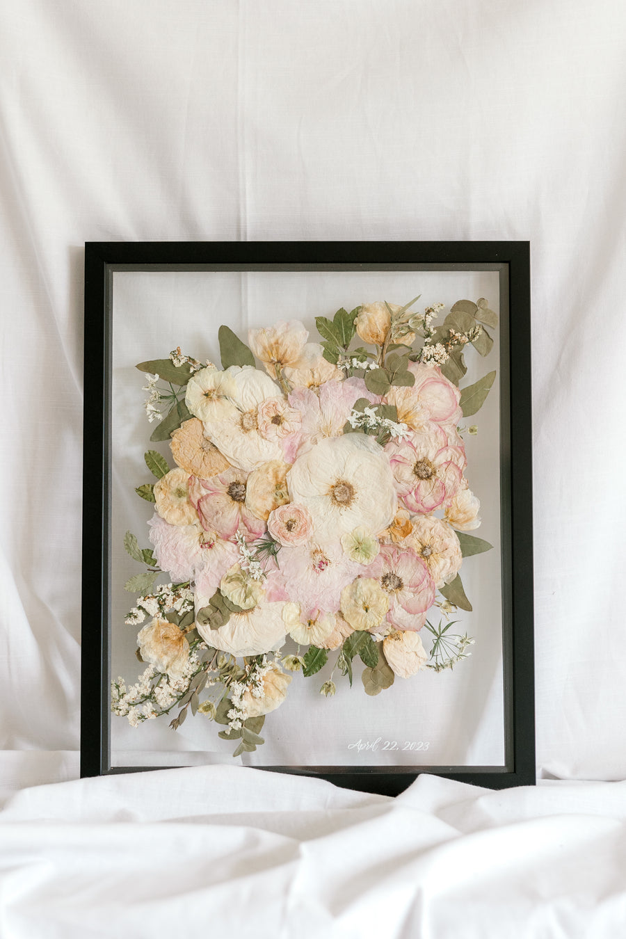 A wedding bouquet pressed and framed inside a black floating frame with a subtle wedding date detail added to the bottom right corner. 