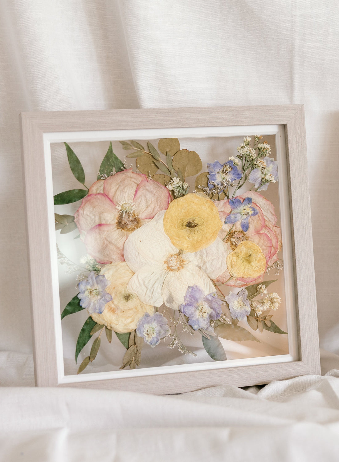 Spring themed pressed flowers preserved in a 10x10 inch floating grey wood frame.