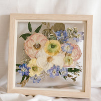 White, pink, yellow, and blue pressed flowers in a 10" square natural wood frame. 