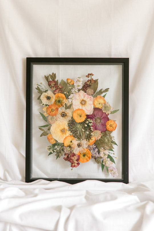 A pressed flower bouquet frame from a wedding on display in glass surrounded by black wood - made by Element Preservation, Previously Pressed Bouquet Shop