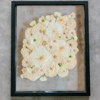 An all white ball bouquet pressed and preserved into a black frame against concrete.