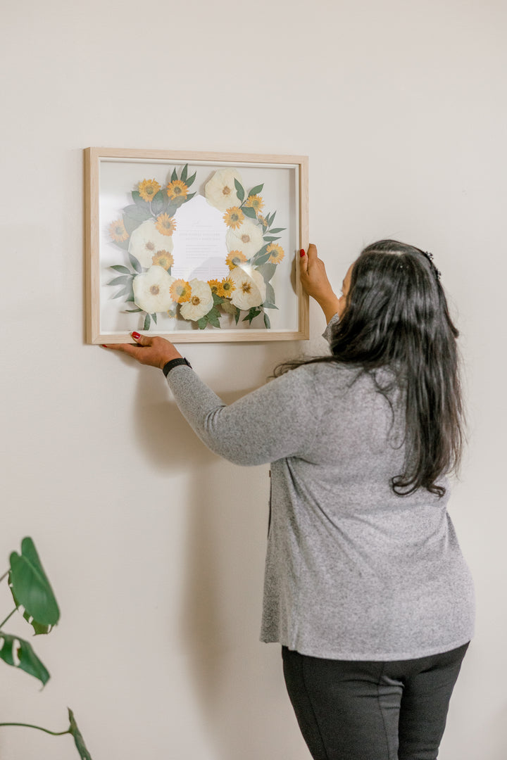 Pressed floral frame with a wedding invitation in the center being hung up by a woman - made by Element Design Co, Element Preservation, Pressed Bouquet Shop 