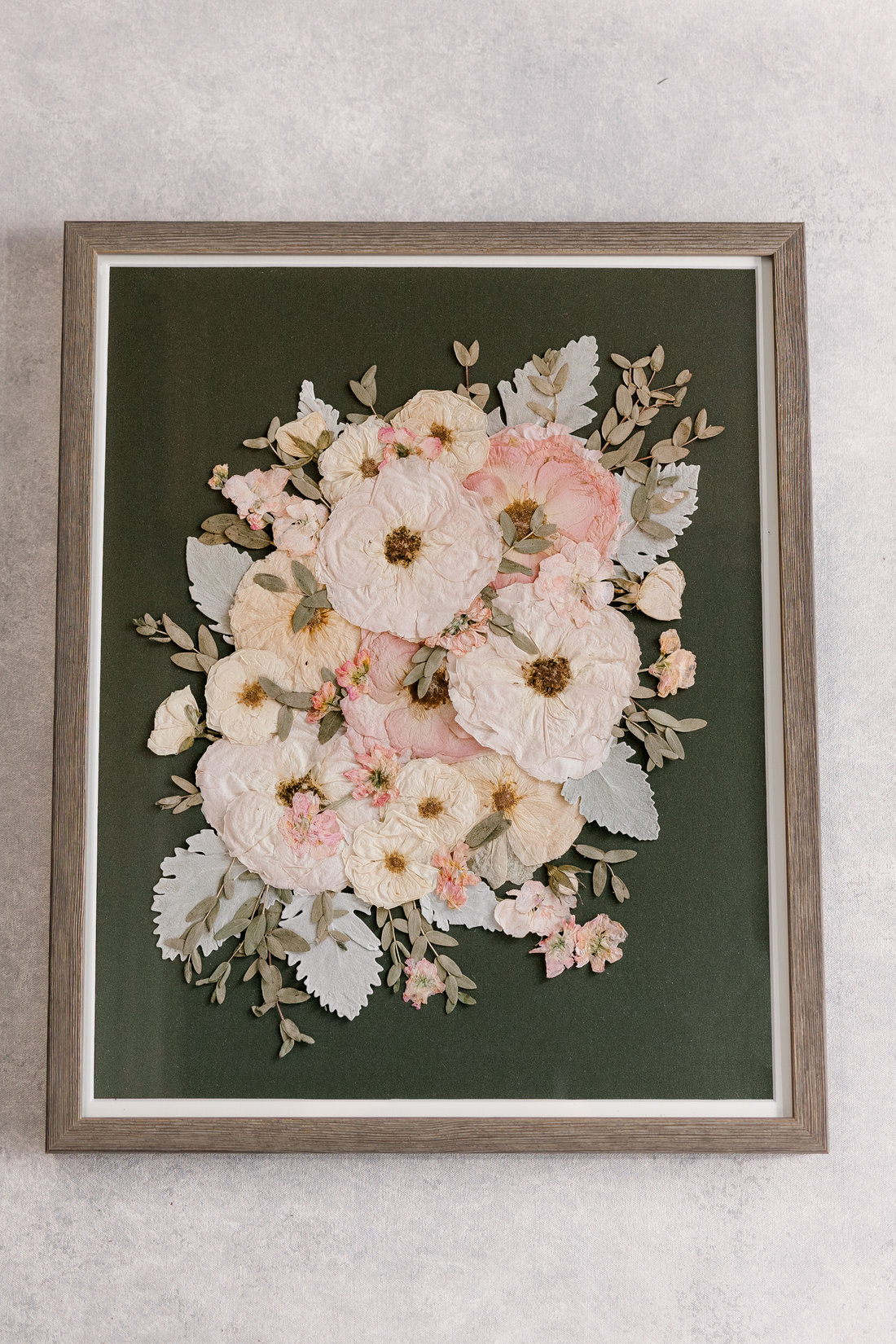 Large wood frame with a green background and pastel pressed flowers inside.