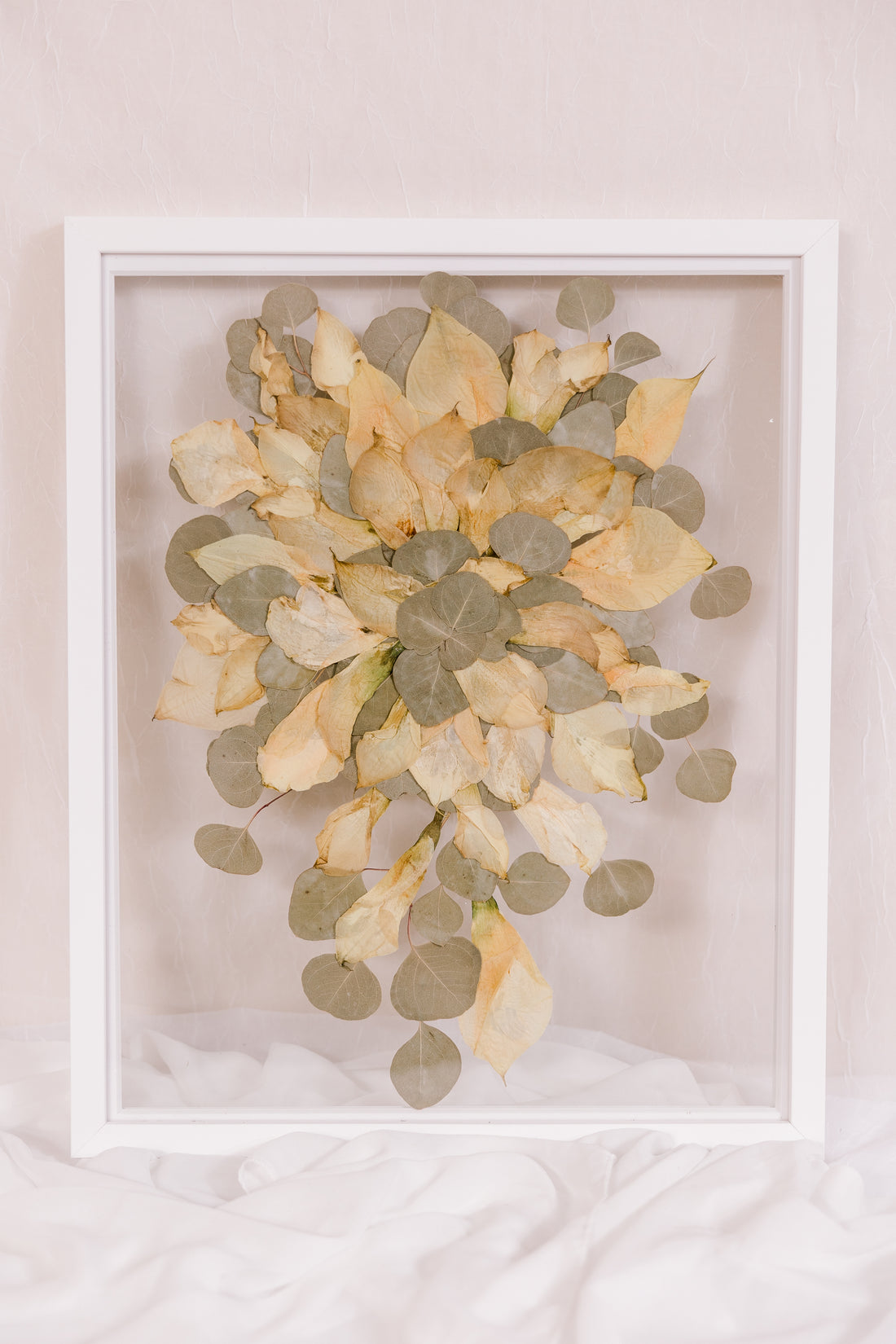 A frame filled with pressed calla lillies displayed in a white wood surround.