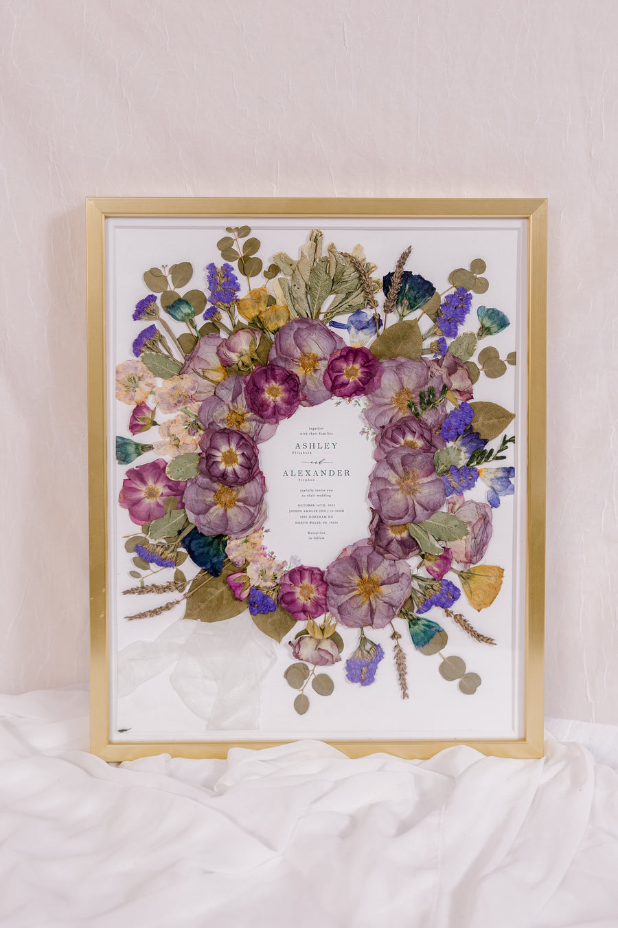 Purple and blue flowers have been pressed and surround an invitation in this bouquet preservation piece. 