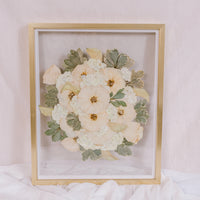 An all white bouquet of flowers has been pressed into a preserved piece of art. 