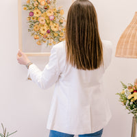 A woman holding a bright flower bouquet that has been pressed and put inside a frame. 