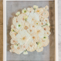 An all white ball bouquet pressed and preserved into a natural wood frame against concrete.