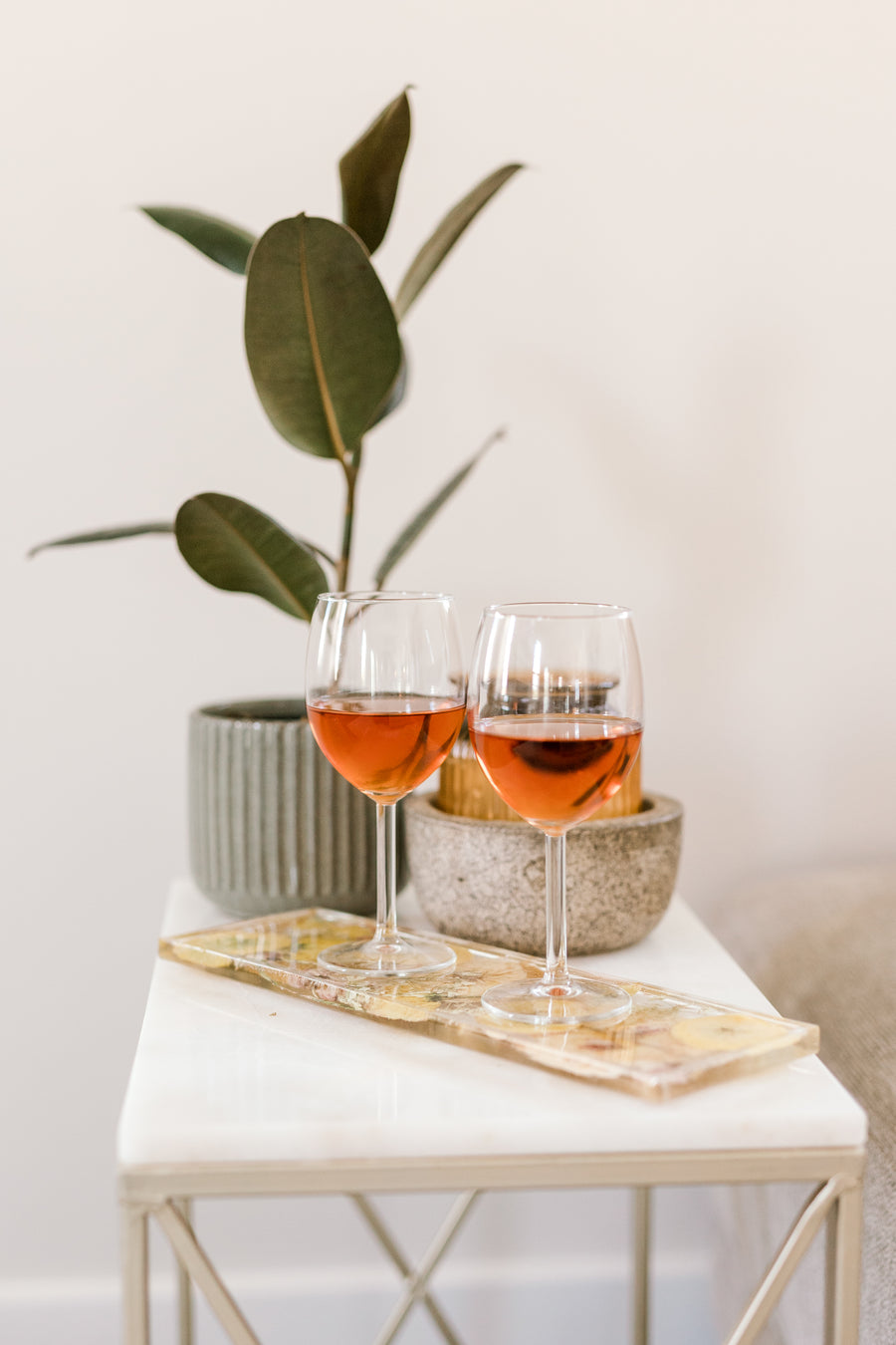 Two glasses of wine sitting on a resin display tray on an end table with a plant in the background. 
