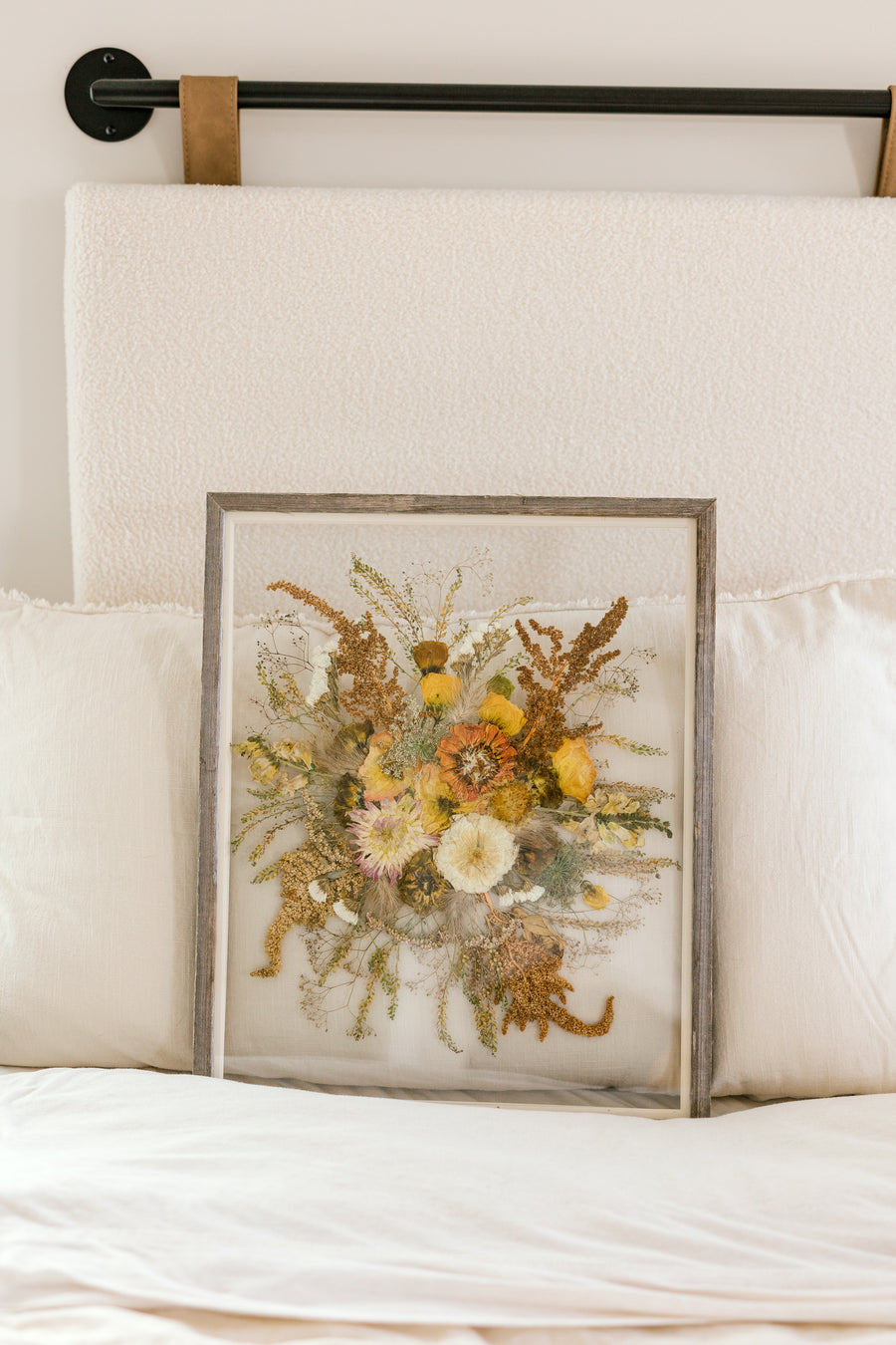 A fall pressed bouquet sitting against pillows on a bed.  