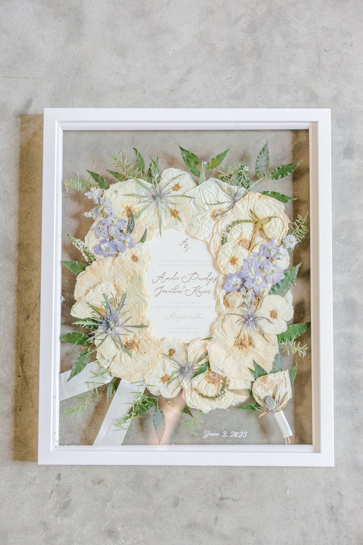 Pressed flower white wood frame with ribbon, silver flakes, invitation, boutonniere, and date additions.