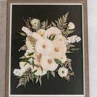 A large wood frame with pressed white and green florals against a black background.