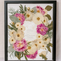 Black wood 16x20 frame with a pressed flower design with wedding invite on white background