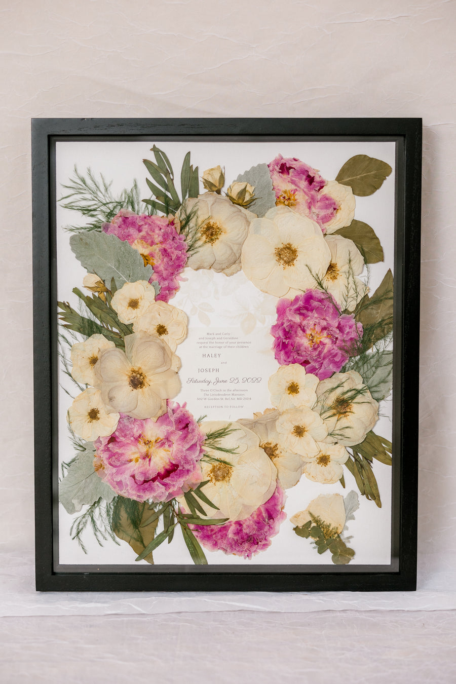 Black wood 16x20 frame with a pressed flower design with wedding invite on white background